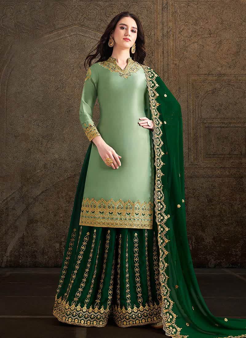 Woman wearing a green traditional outfit with gold embroidery against a textured wall.